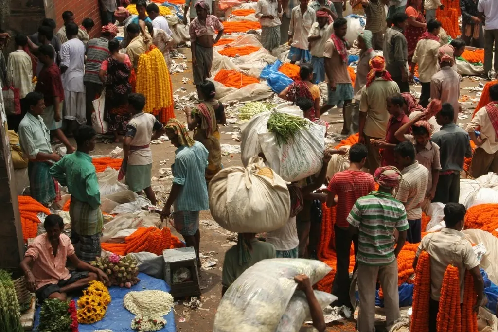 Traders carrying sacks and garlands through a busy Kolkata market